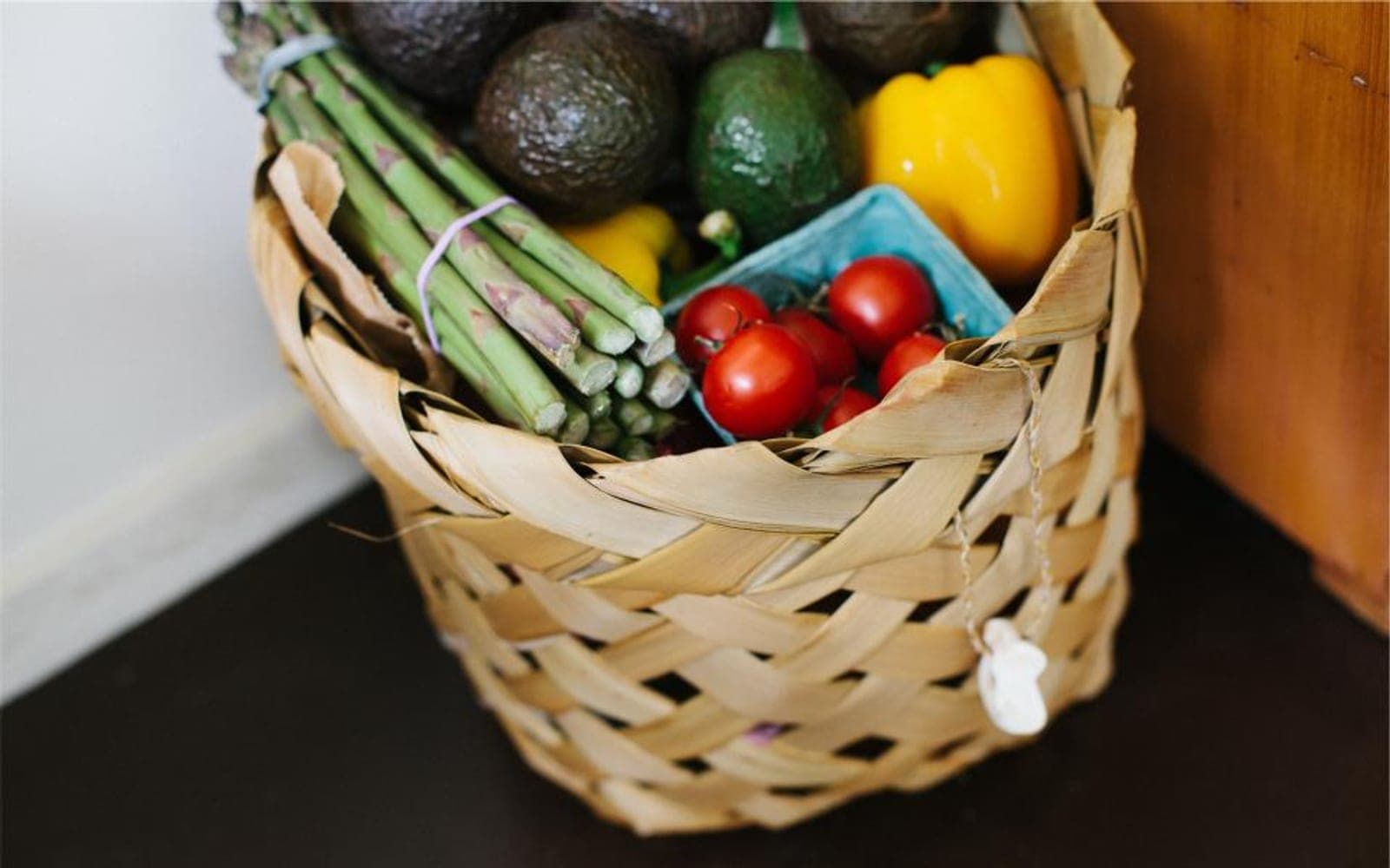 Cesta trançada com aspargos, abacate, pimentão amarelo e tomates