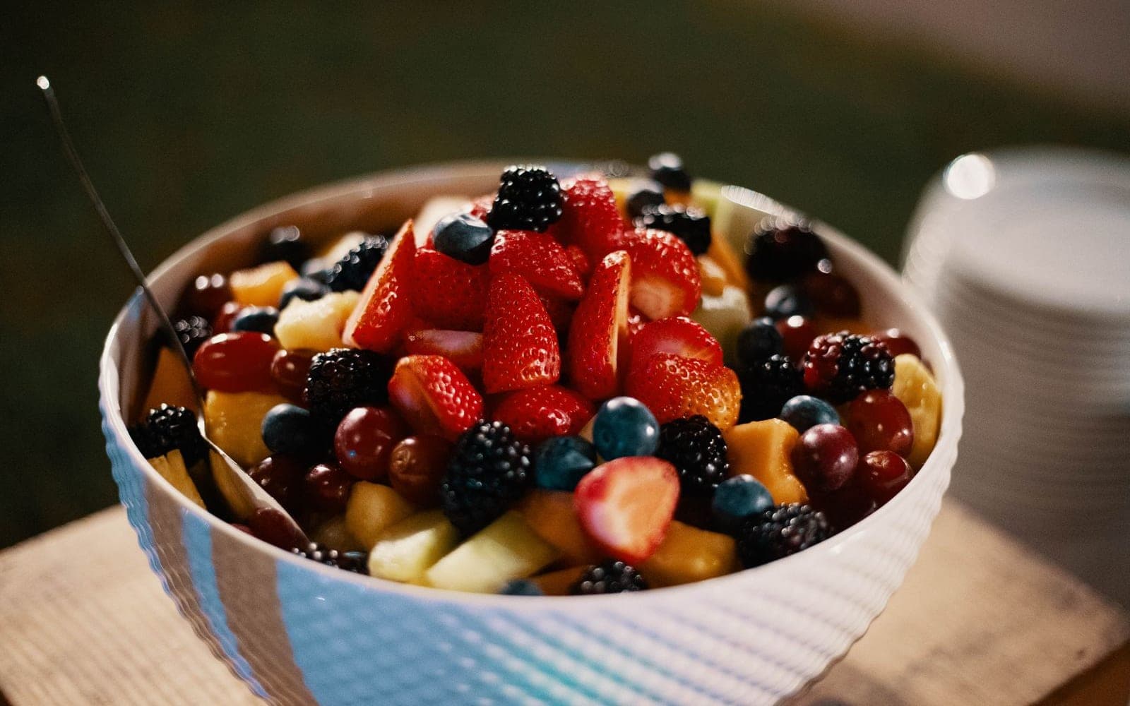 Tigela de frutas variadas com morangos, mirtilos e banana fatiada sobre uma tábua de madeira