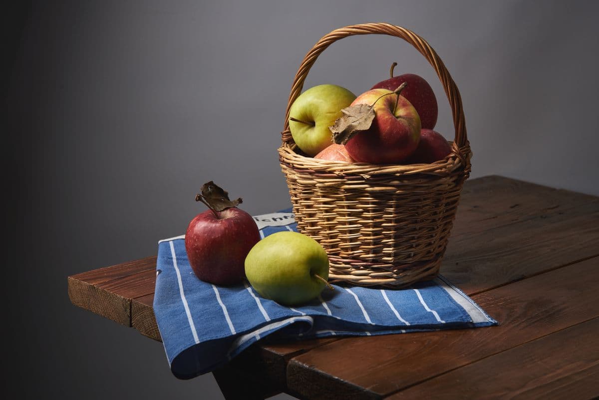 Cesta de vime com maçãs vermelhas e verdes sobre mesa de madeira