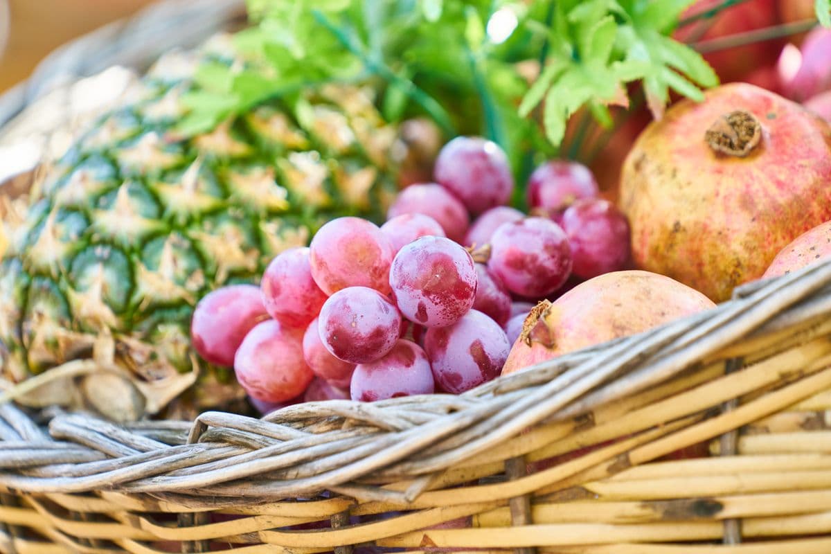 Uvas, abacaxi e romãs em cesta de vime