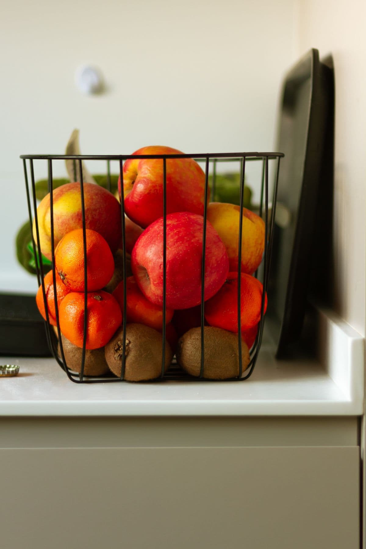 Cesta de arame com maçãs, tangerinas e kiwis sobre a bancada da cozinha