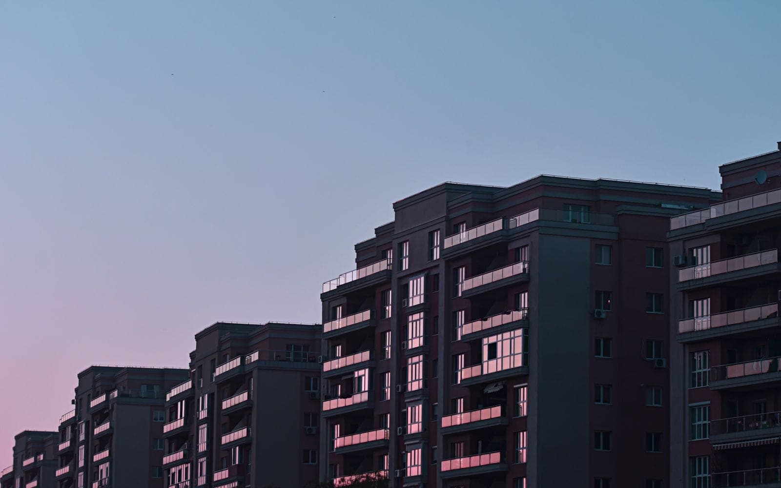 Fileira de prédios residenciais ao entardecer, com o céu em tons de azul e rosa