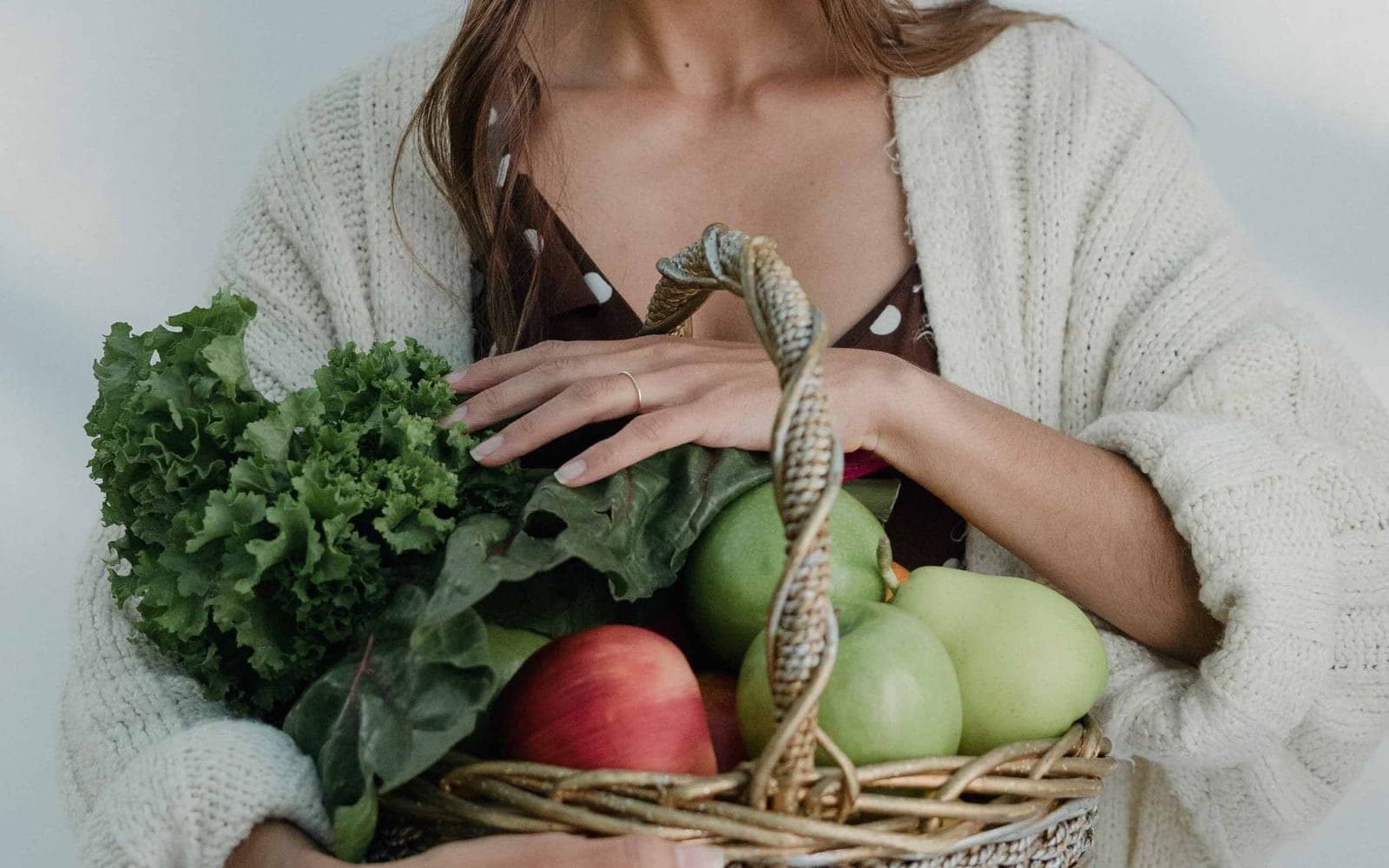 Mulher segurando verduras frescas e legumes junto ao corpo, em um ambiente claro