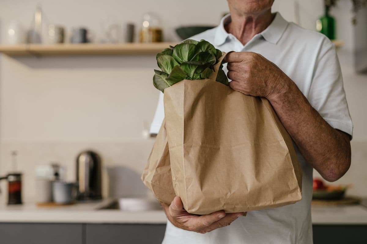 Homem segurando uma sacola de papel cheia de verduras na cozinha