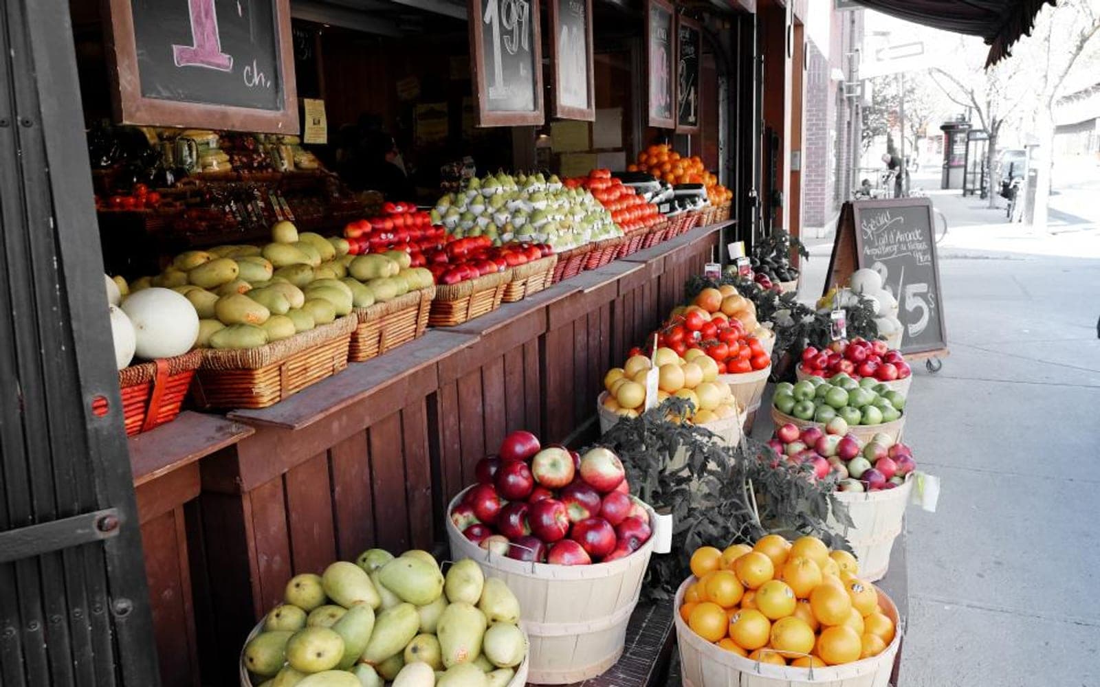 Banca de frutas e verduras em cestos de madeira na calçada de uma rua