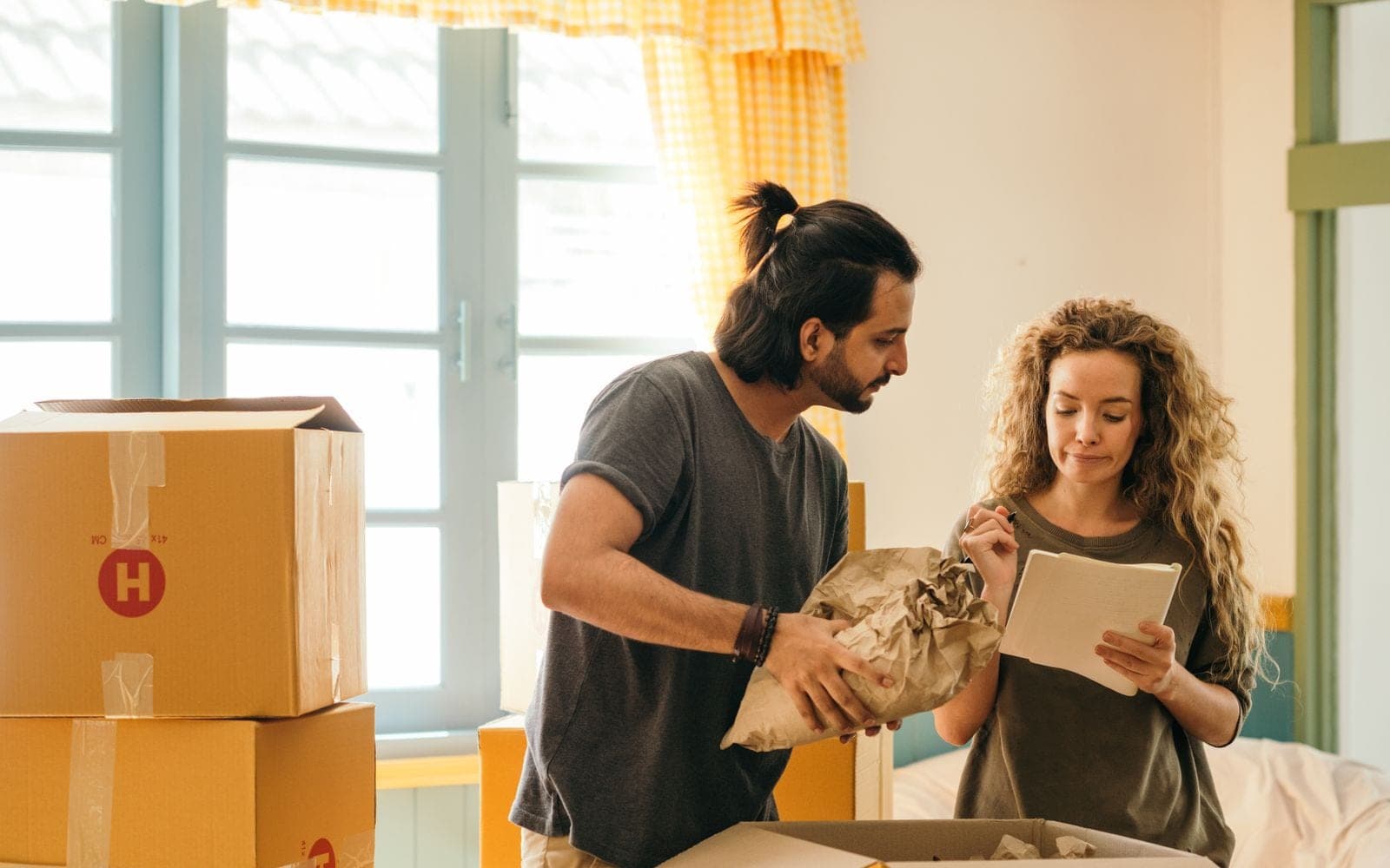 Casal confere uma encomenda em casa ao lado de caixas de papelão, com uma prancheta