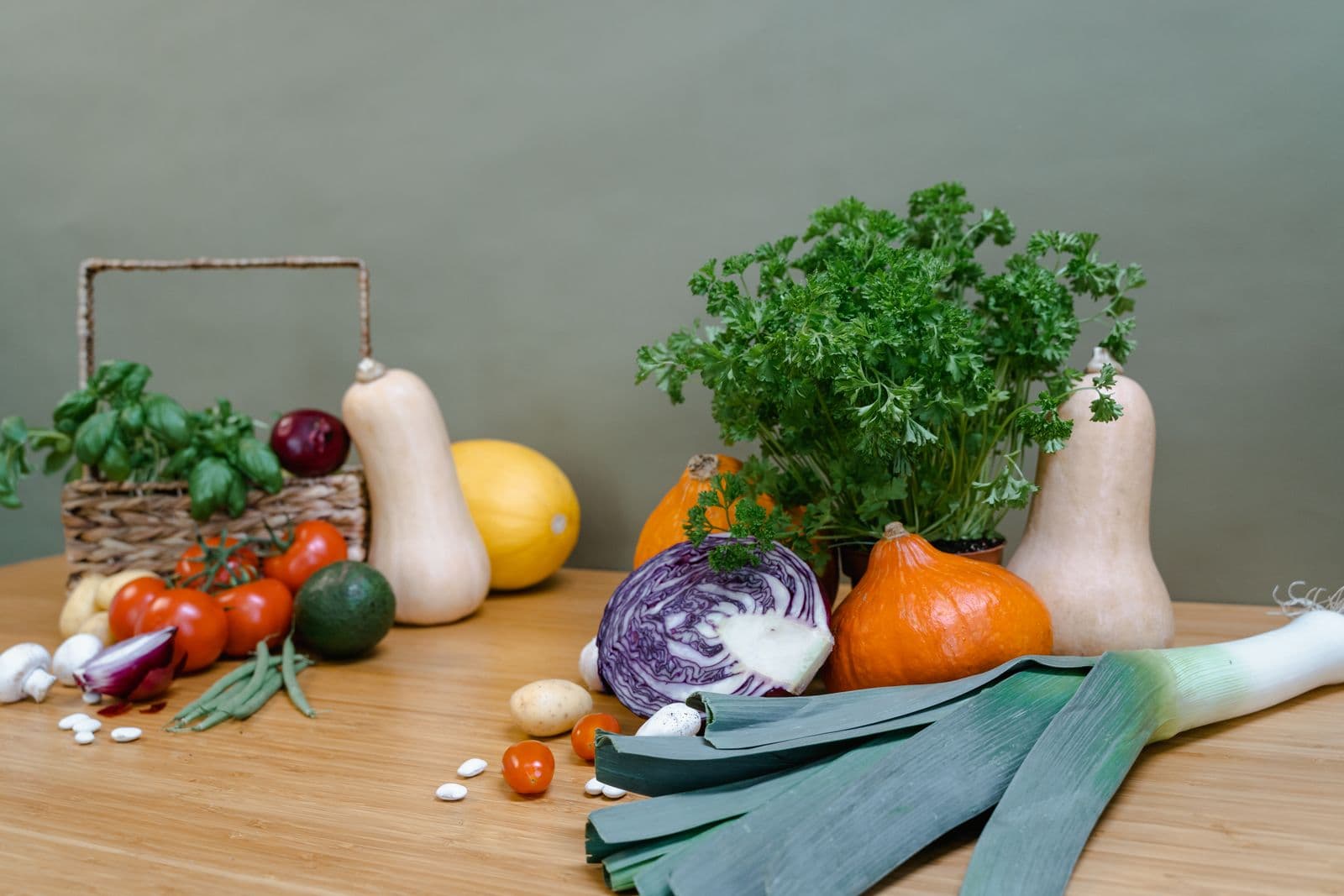 Tomates, abobrinhas, repolho roxo e ervas frescas organizados sobre uma bancada de madeira