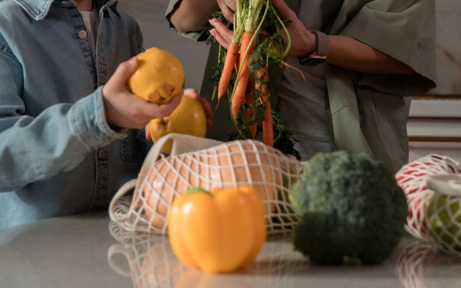 Mãe e filho desembalando verduras e cenouras sobre a mesa da cozinha