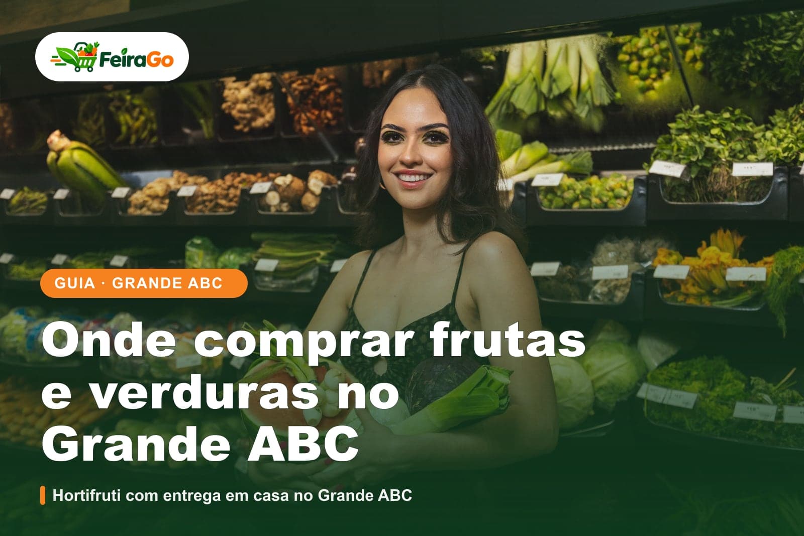 Mulher sorridente de cabelos escuros segurando melancia, folhas e legumes diante de prateleiras de verduras num sacolão