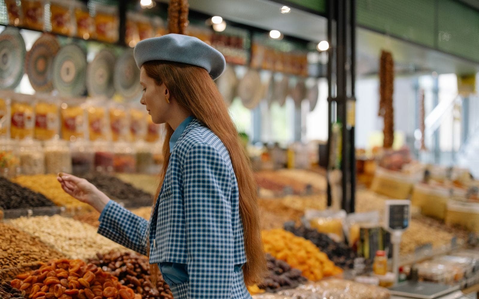 Mulher de boina azul escolhendo castanhas e frutas secas numa banca de mercado