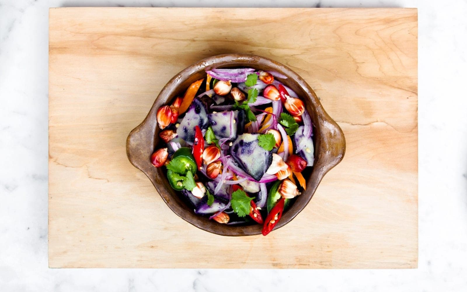 Tigela de barro com salada colorida de folhas, cebola roxa e pimentão sobre uma tábua