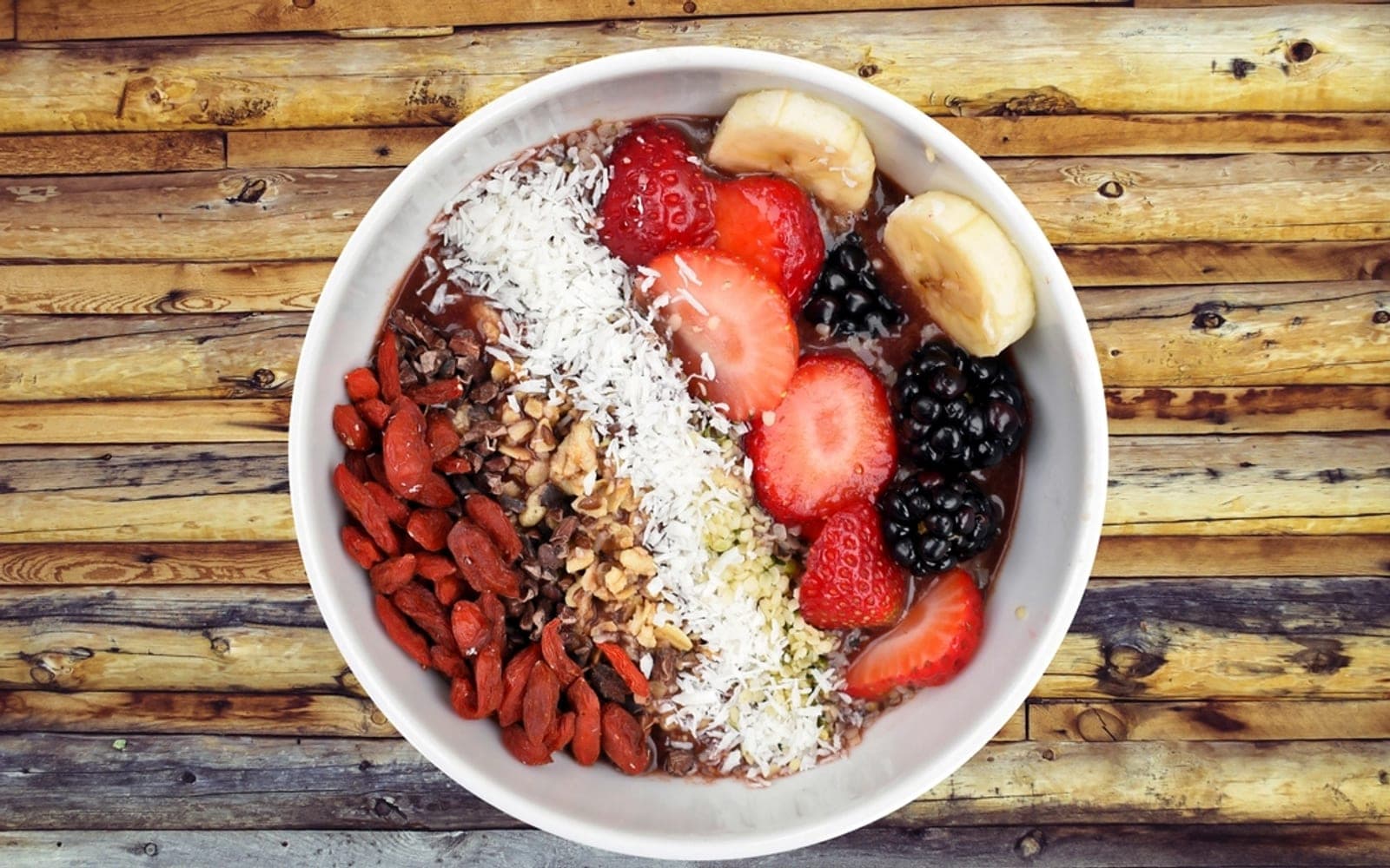 Tigela com morangos, amoras, banana, coco ralado e frutas secas
