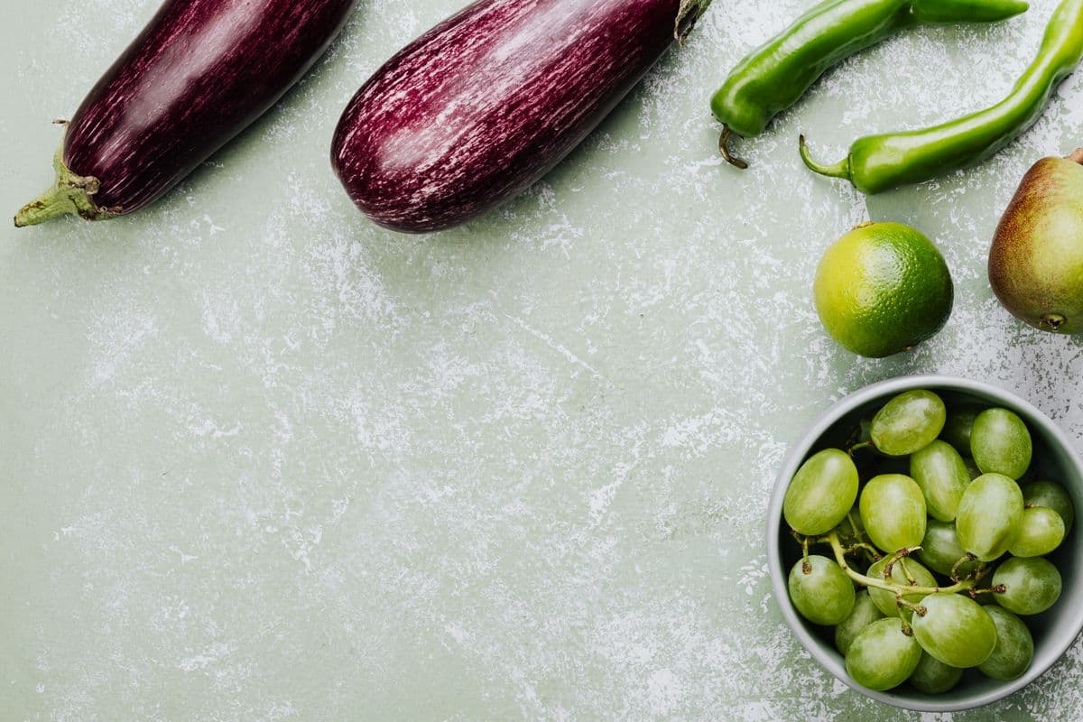 Berinjelas, pimentas verdes, limão, pera e uvas verdes sobre fundo claro