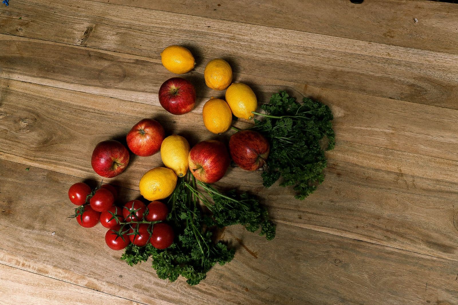 Maçãs, limões, tomates e salsinha sobre uma mesa de madeira