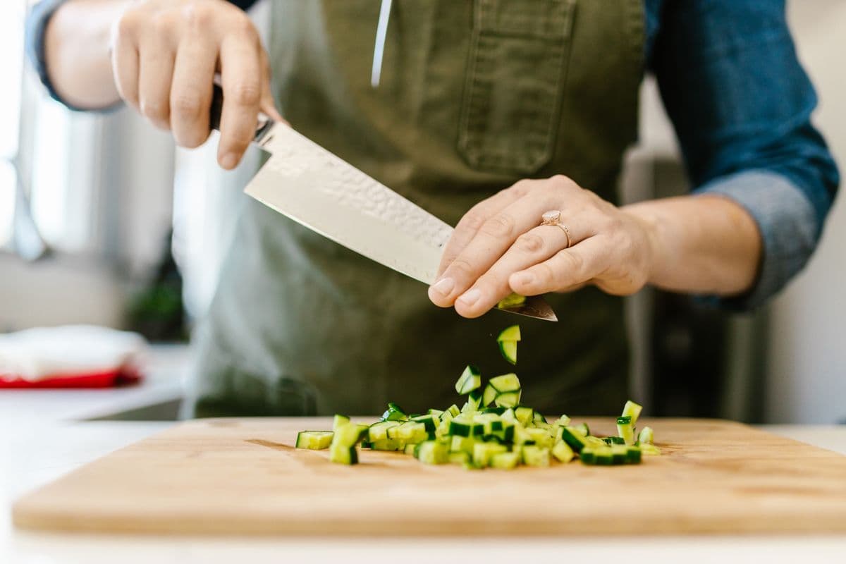 Chef cortando pepino em fatias finas sobre tábua de madeira