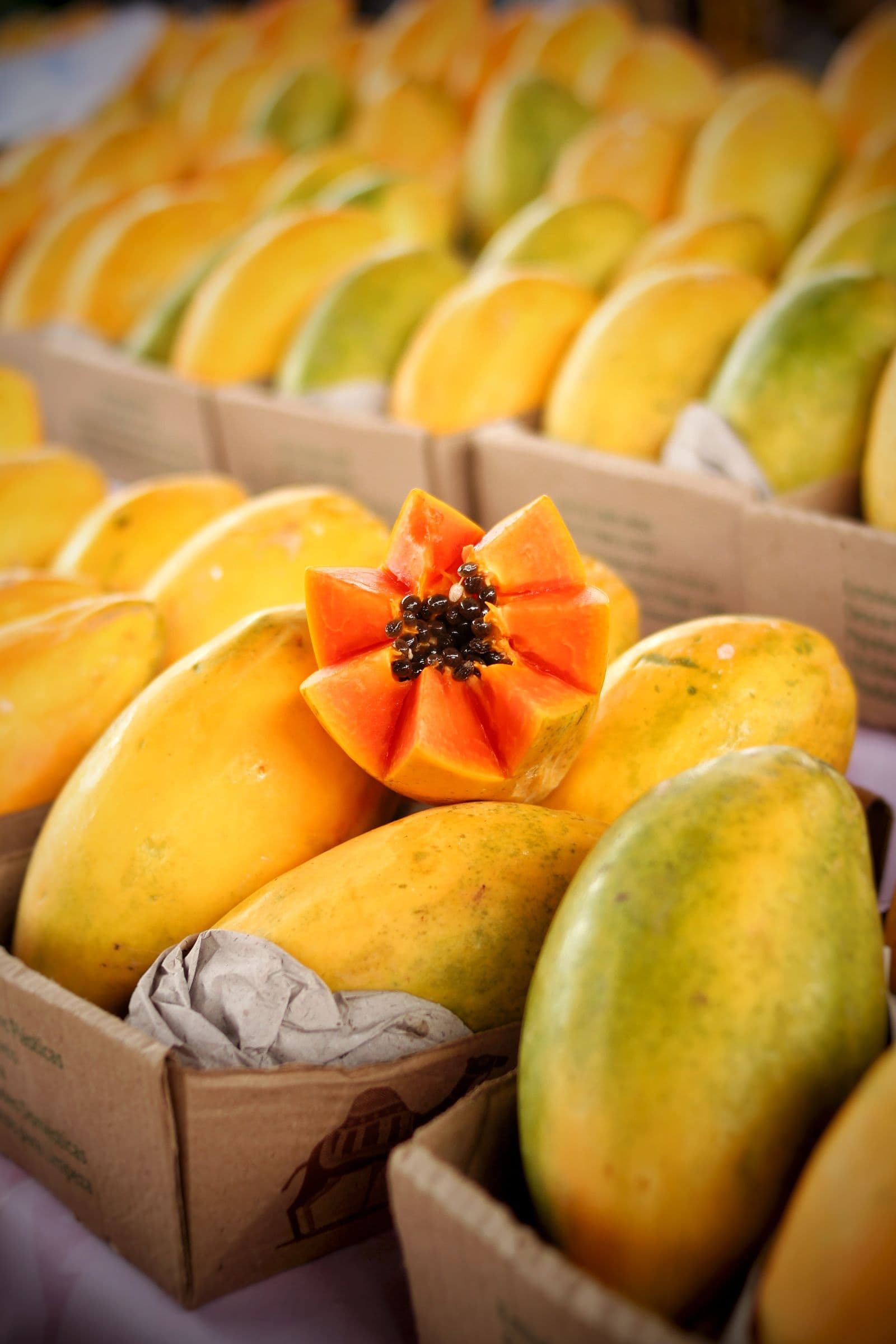 Mamões papaia em caixas numa banca de feira, com um mamão cortado em forma de flor