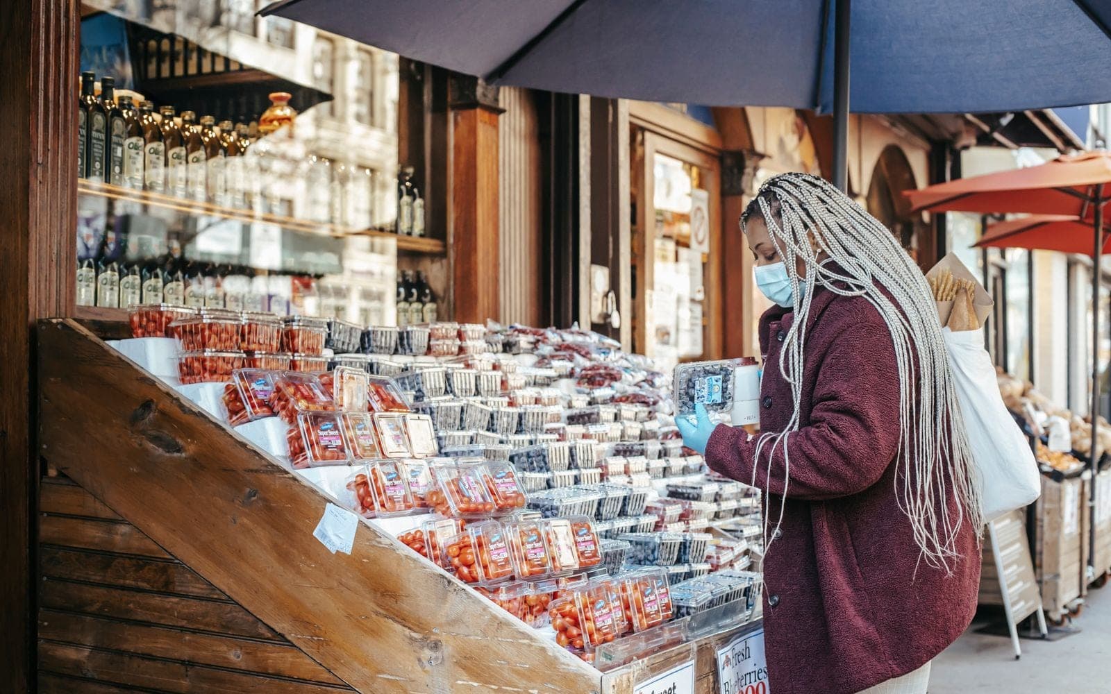 Mulher com máscara escolhendo morangos em uma banca de rua cheia de frutas