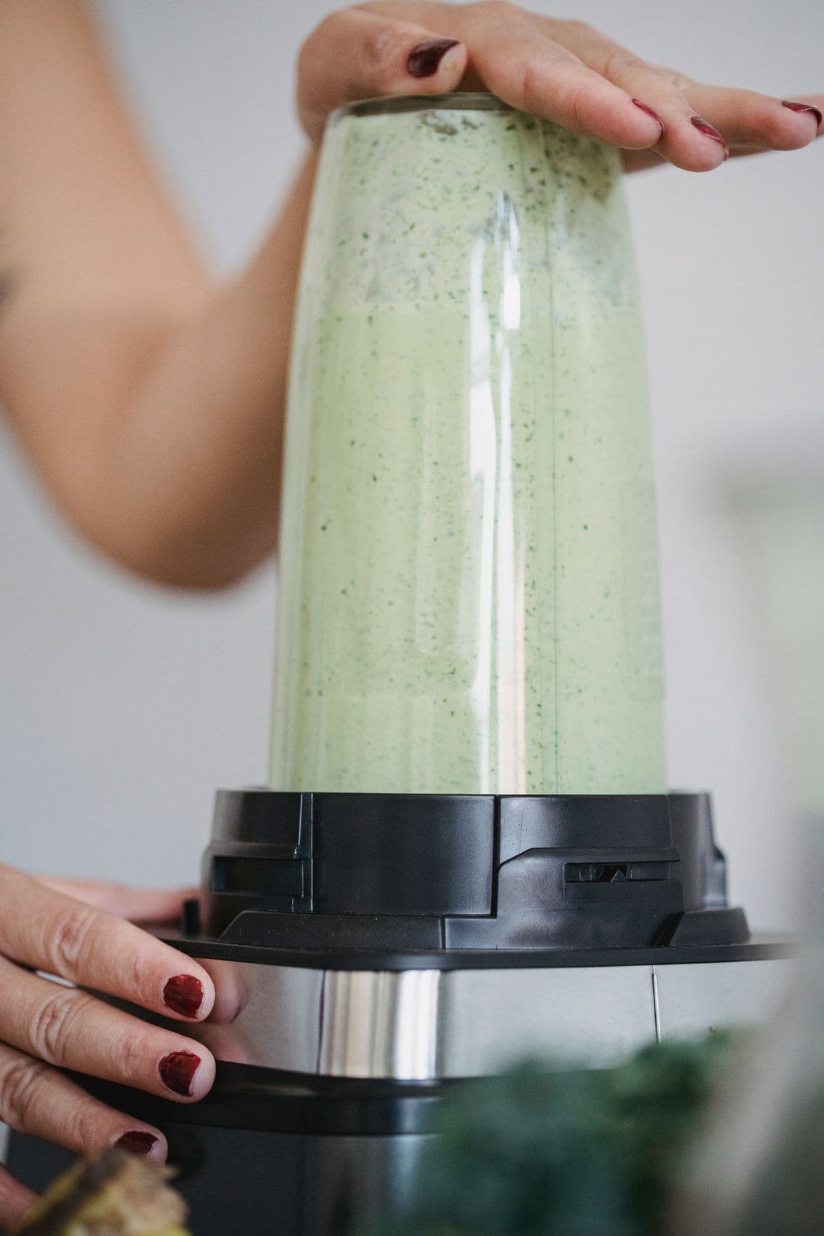 Mãos segurando o jarro de um liquidificador cheio de vitamina verde cremosa