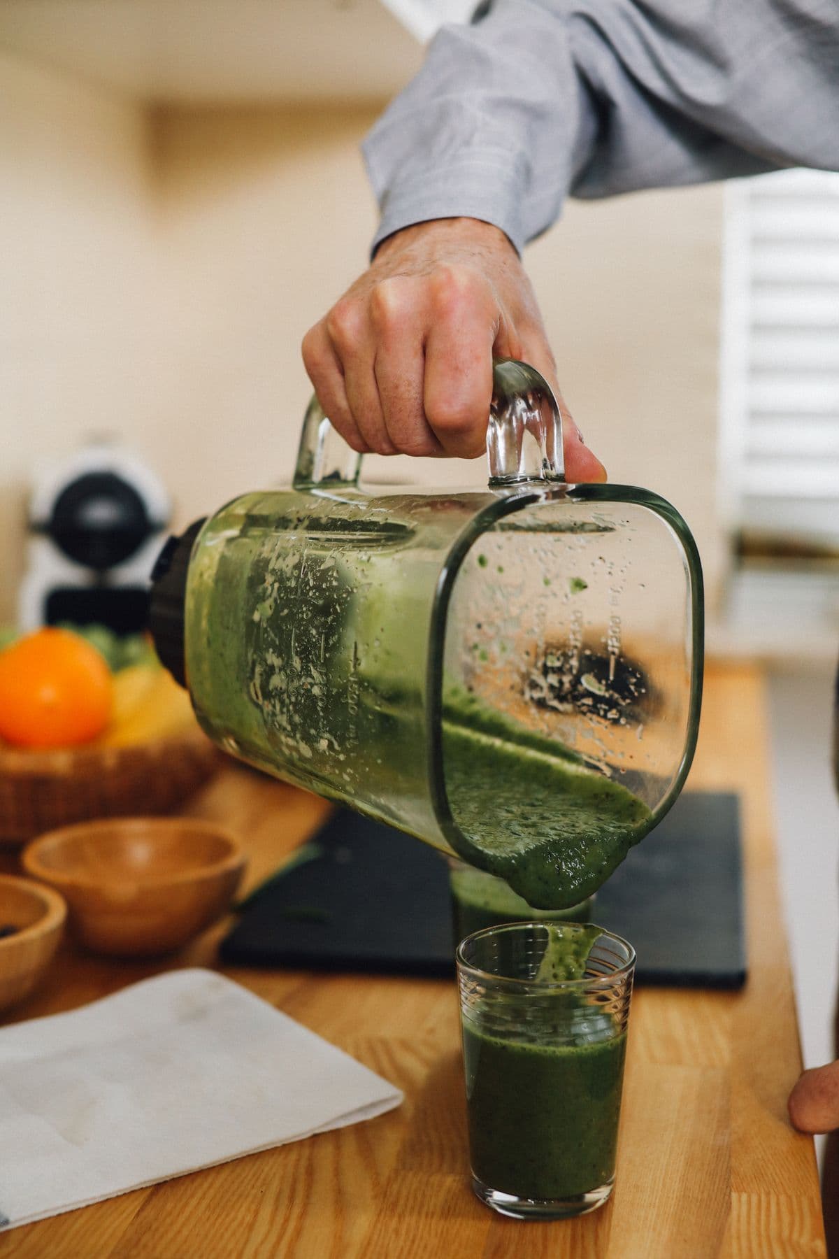 Suco verde sendo servido de um jarro de vidro em um copo sobre a bancada da cozinha